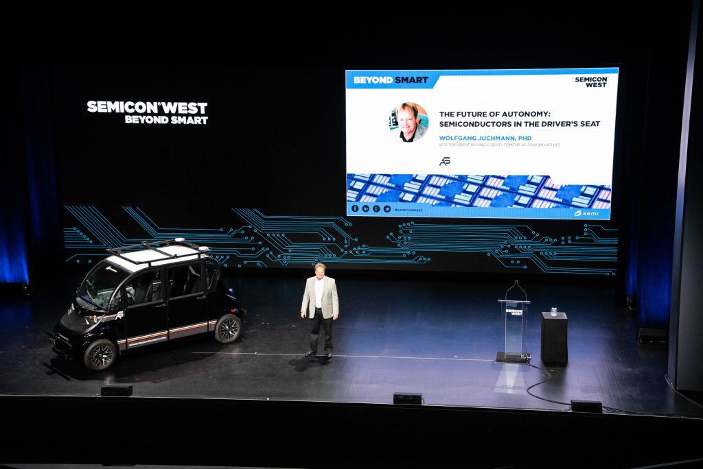 Someone presenting on a stage with a vehicle and a screen